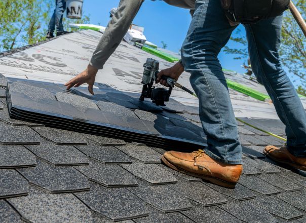 Roofer using nail gun for shingle installation on residential roof.